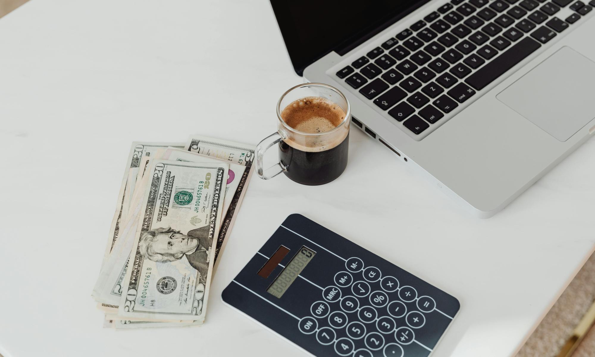 Person budgeting at a modern desk with coffee, laptop, calculator, and money – personal finance planning
