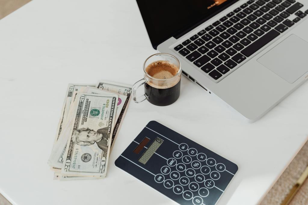 Person budgeting at a modern desk with coffee, laptop, calculator, and money – personal finance planning